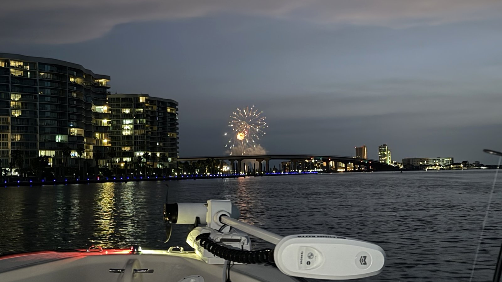 The bow of a skiff on calm water at dusk with the Orange Beach skyline lit up across the pass